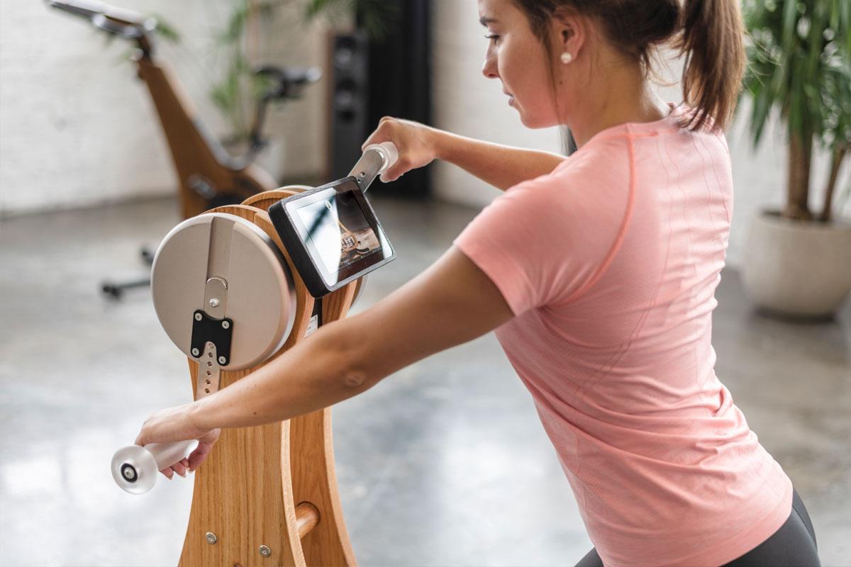 Frau trainiert an Fitnessgerät mit Bildschirm, Holzdesign sichtbar.