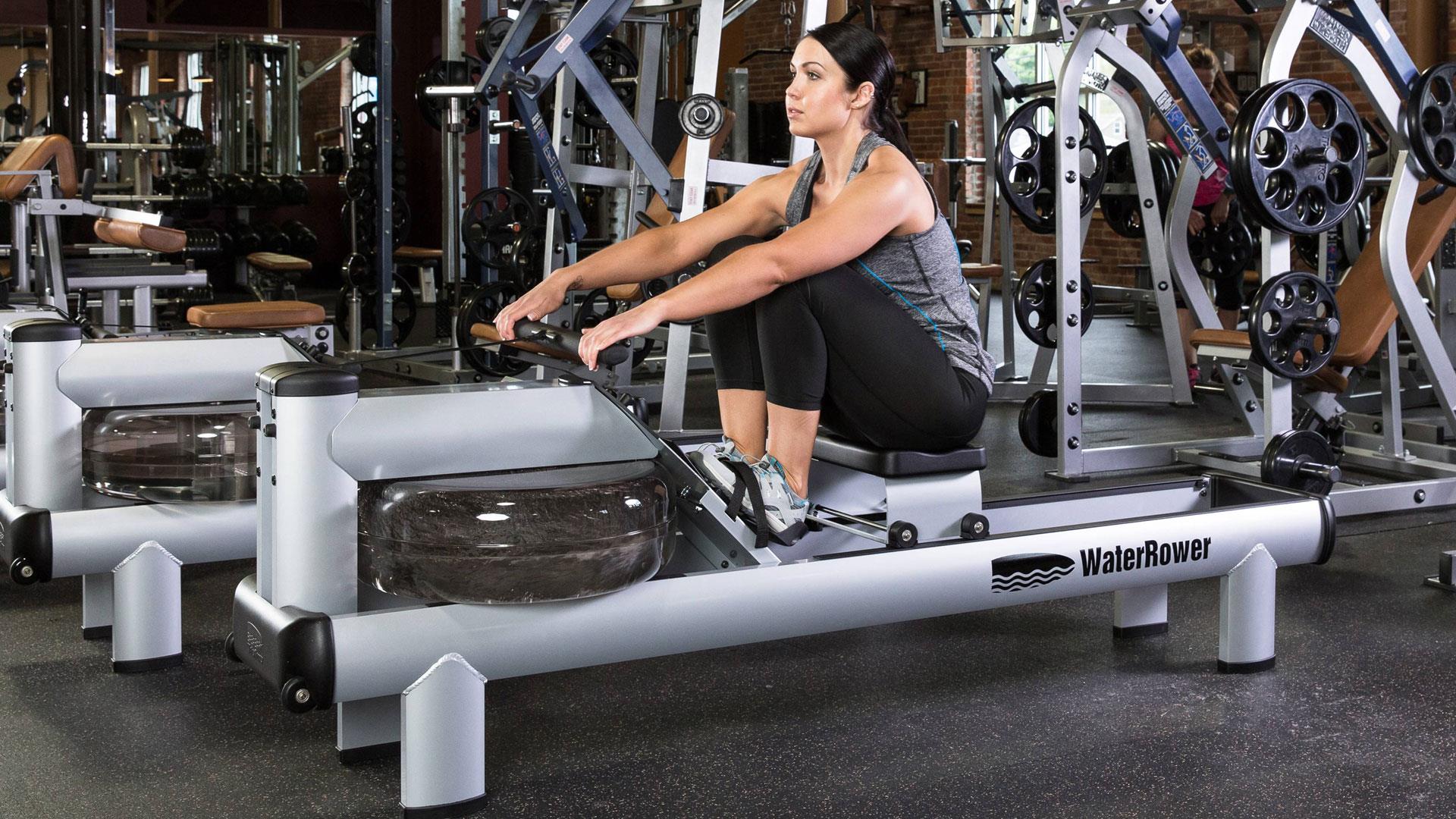 Person auf WaterRower-Rudergerät im Fitnessstudio.