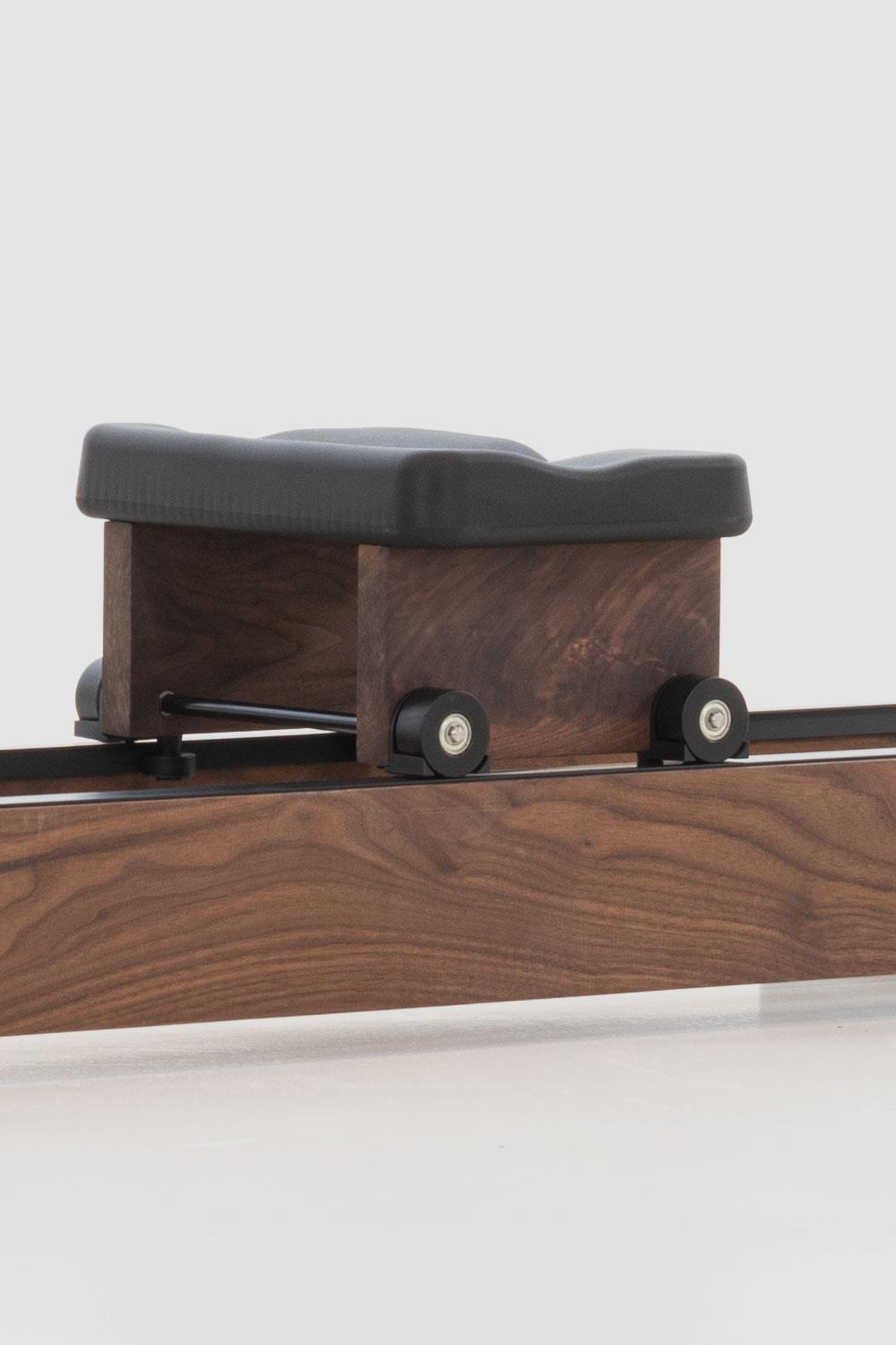 Holz-Rudergerät mit schwarzem Sitz und Rollen auf Schiene.